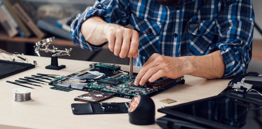 Laptop disassembling with screwdriver at repair shop. Engineer fixing broken computer motherboard. Electronic renovation, technology development concept