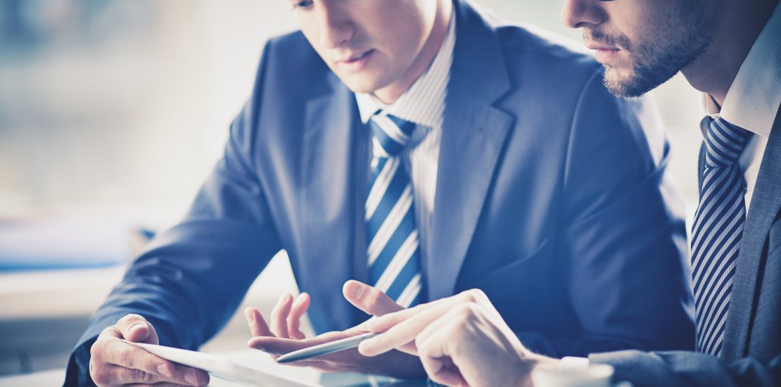 Image of two young businessmen discussing document in touchpad at meeting